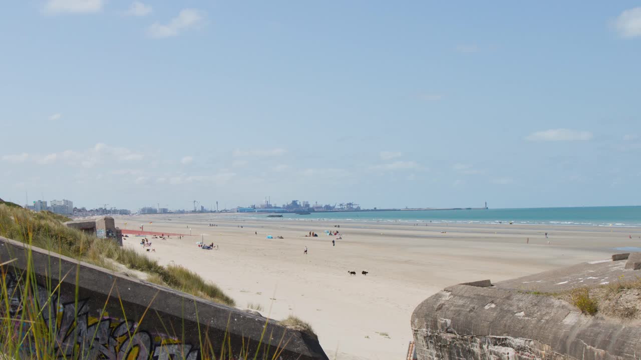 Camera pans across historic bunker, sandy dunes, and coastline under bright daylight at Dunkirk beach