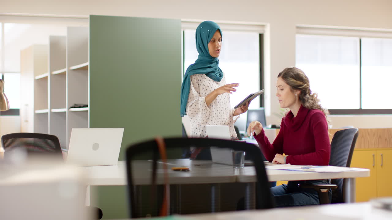 다양한 여성 창의적인 동료들이 사무실에서 노트북과 태블릿을 사용하여 토론하고, 느린 동작
