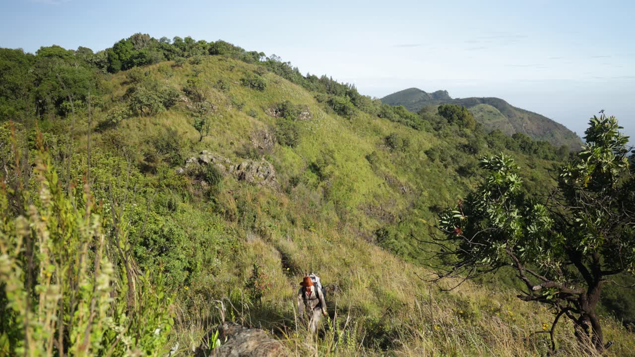 un hombre occidental caminando a lo largo de una cordillera montañosa en áfrica oriental con increíbles vistas tropicales