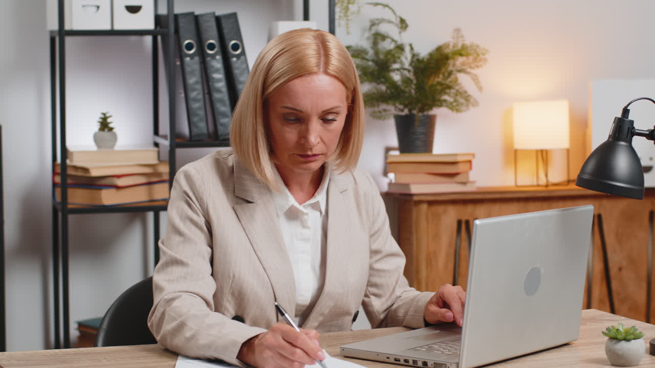 노트북을 사용하는 성숙한 사업가 여성이 가정 사무실 책상에서 금융 그래프 문서를 작업합니다.