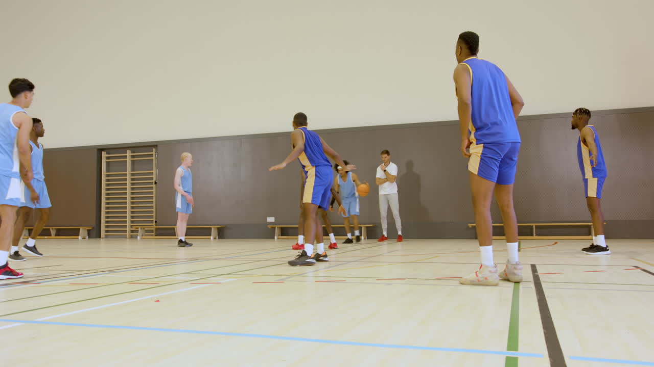 Jogadores de basquete competindo intensamente em quadra coberta durante jogo de treino.