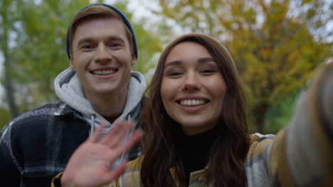 cheerful young couple waving hands on selfie video outdoors