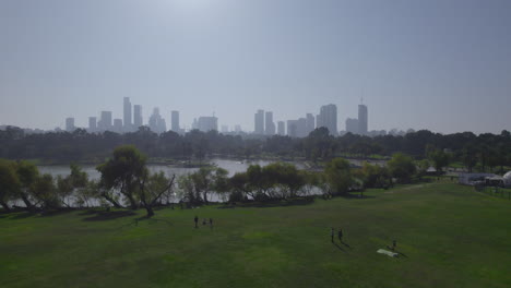 Revealing-the-Tel-Aviv-towers-from-the-lawns-of-Yarkon-Park-,-a-huge-stretch-of-greenery-in-the-center-of-Tel-Aviv-for-picnic,-rent-a-bike,-rent-a-boat,-water-park-and-playgrounds