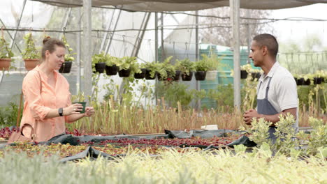 woman tending plants in greenhouse, smiling and engaging with coworker