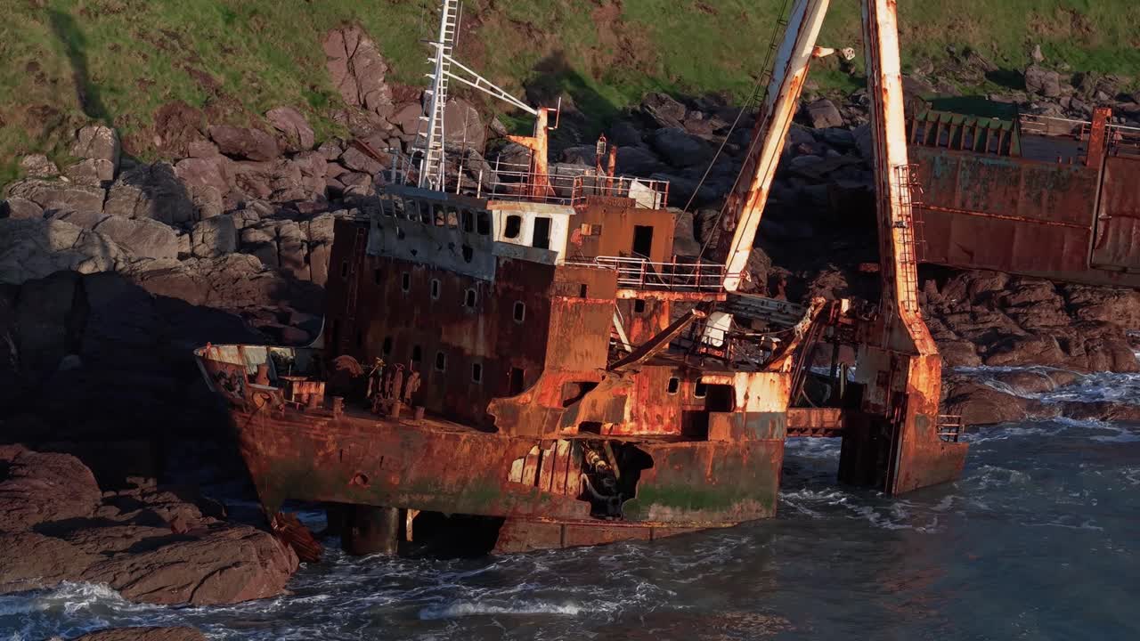 A rusted fishing boat wreck stranded on rocky shores during golden hour in Ireland