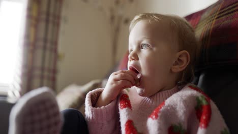 niño pequeño británico comiendo bocadillos en un sofá, en una sala de estar