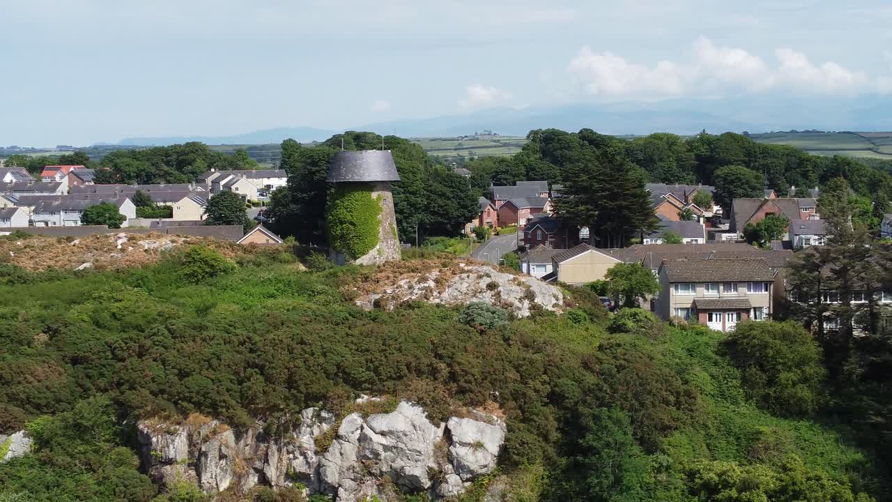 llangefni molino de viento cubierto de hiedra en la ladera del punto de referencia vista aérea orbitando el campo de snowdonia galés, anglesey