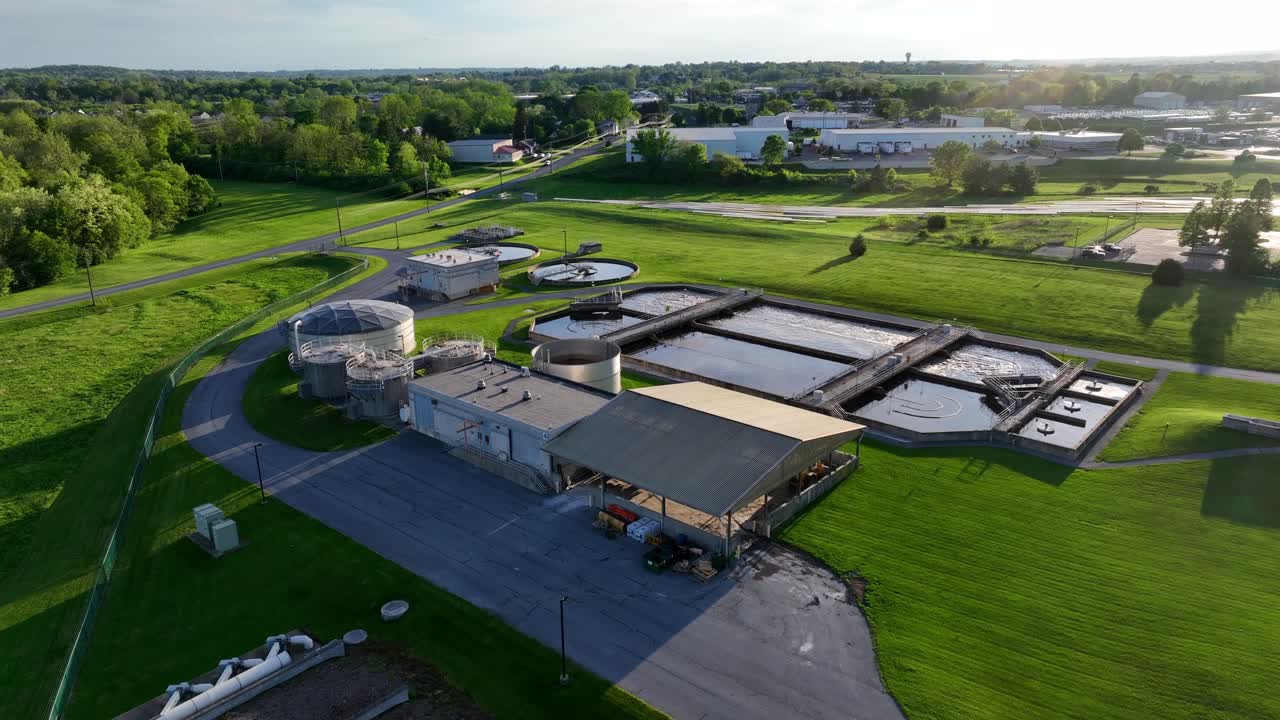 Water purification and sewage treatment plant in american town during golden sunset. Aerial approaching wide shot. Green grass surrounding company.