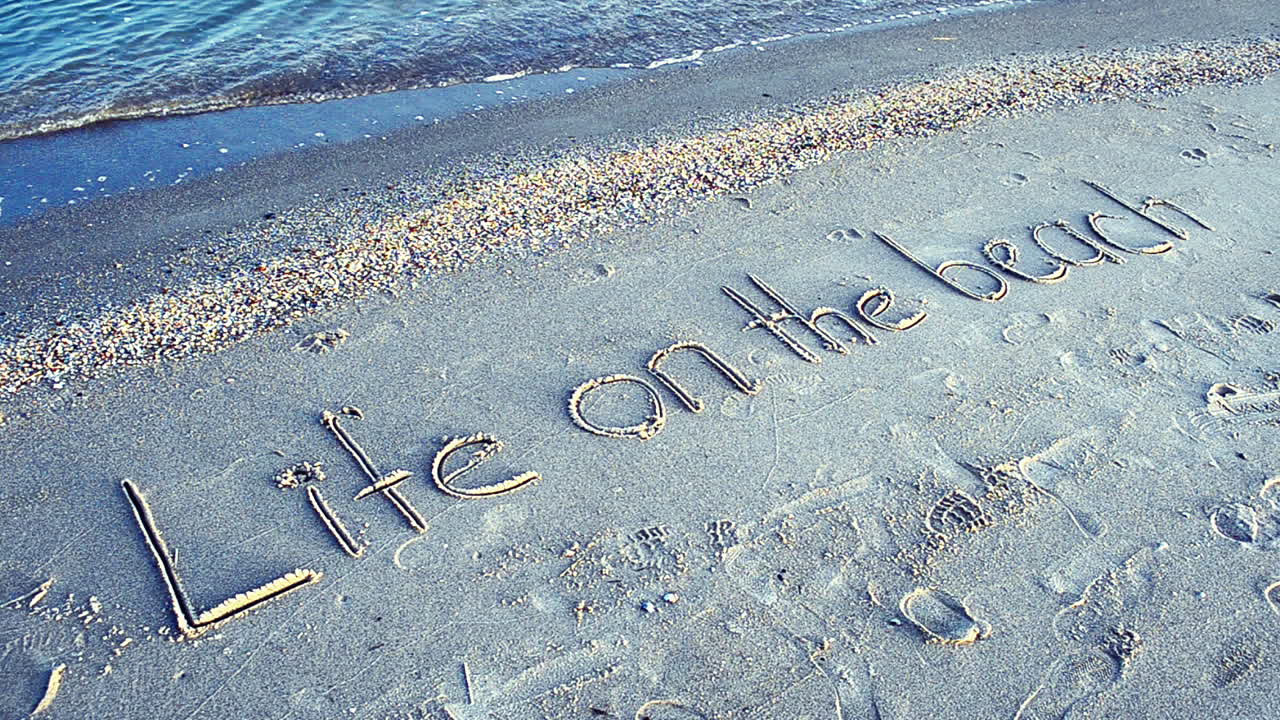 Filmagem na praia. Conceito de vida na praia - inscrição na areia da praia com uma onda se aproximando