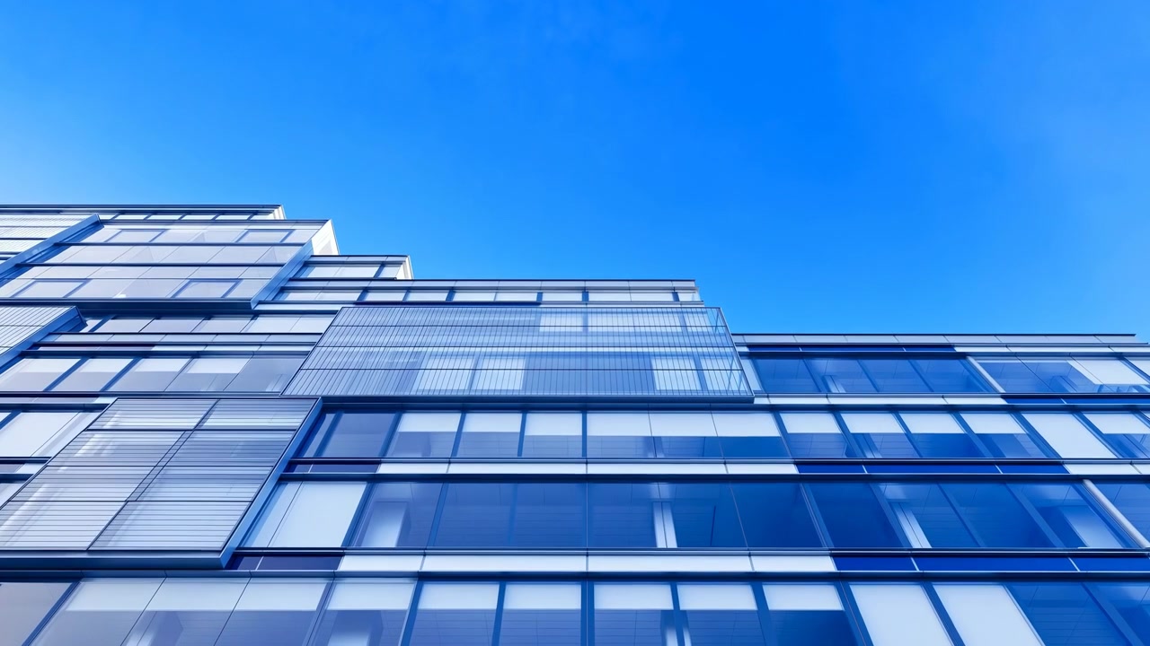 Edificio moderno per uffici con facciata in vetro e cielo azzurro, che incornicia una vista verso l'alto di un'elegante sede aziendale, riflettente.