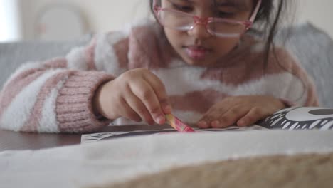 young girl drawing with crayons at a table