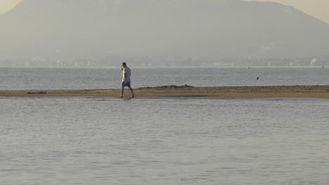 young man walking barefoot alone on sandy shoreline, early morning