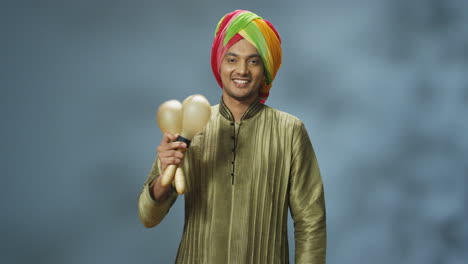 Close-up-view-of-cheerful-Indian-man-in-traditional-clothes-and-turban-playing-maracas-and-smiling-at-the-camera