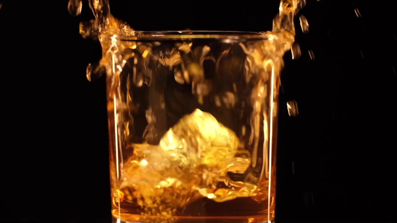 Nærbillede af whisky med en isterning, der falder ned i et glas whisky eller anden alkohol i slowmotion