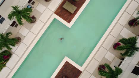 drone top shot of a girl swimming in the pool at the blue luxury hotel, tulum