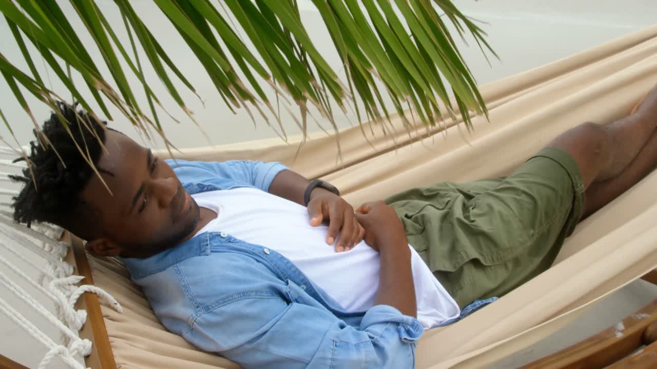 High angle view of African american man sleeping in a hammock at beach 4k