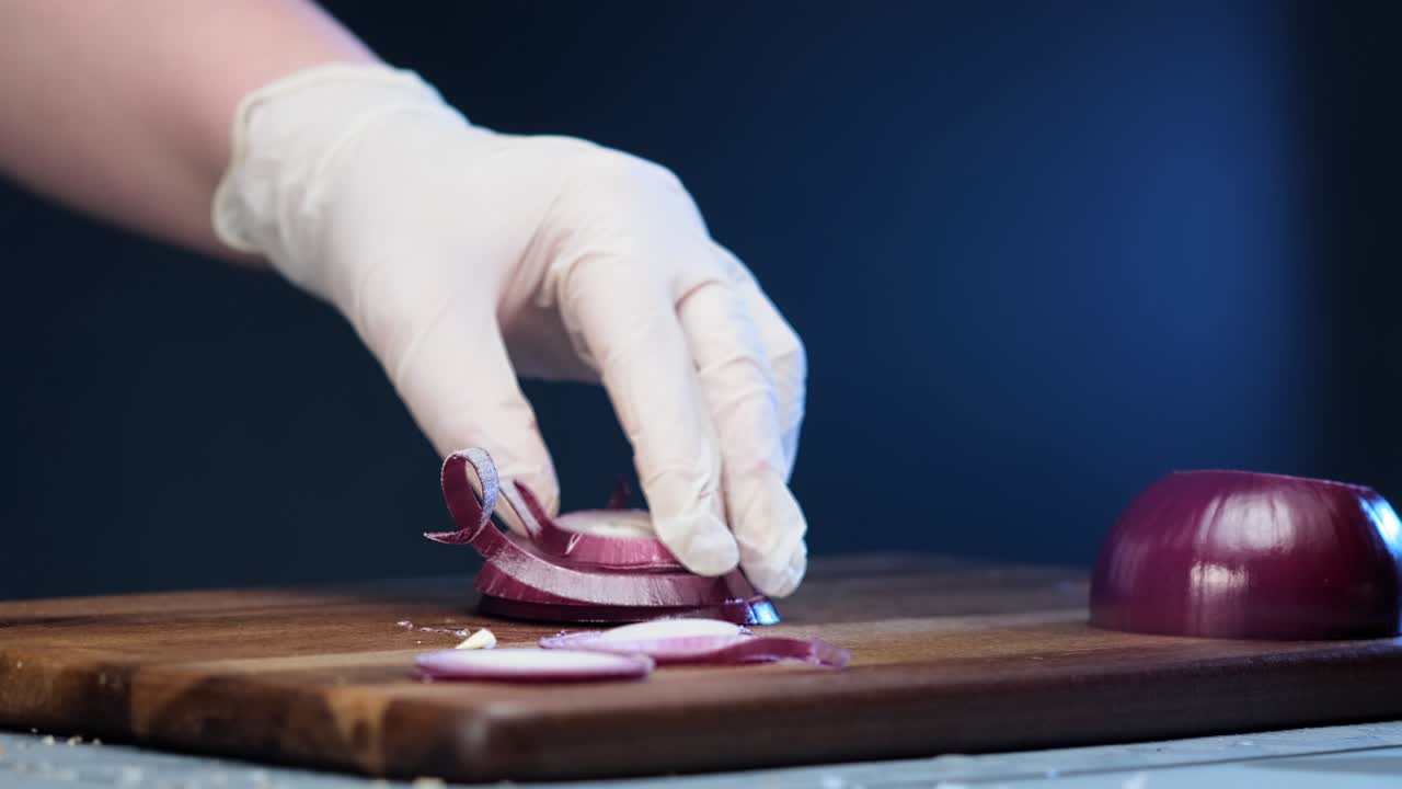 Person in white gloves cuts red onion into small thin slices
