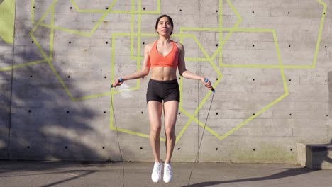 Young-Latina-Woman-using-jump-rope-by-concrete-wall,-Wide-Shot