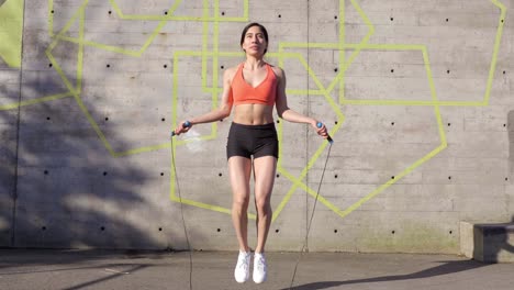 young latina woman using jump rope by concrete wall, wide shot