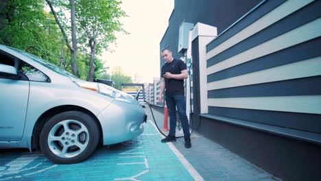 proceso de reabastecimiento de combustible de un automóvil eléctrico. un disparo debajo de la escotilla donde se carga el automóvil ecológico eléctrico. la escotella de carga del automóvil eléctrico se abre automáticamente. una mano masculina inserta un automóvil erecto