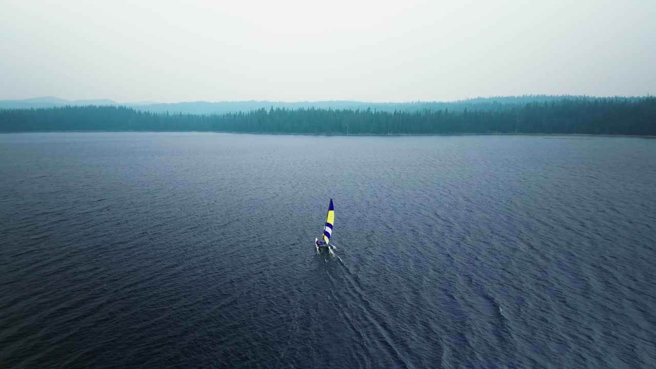 un barco de vela solitario se enfrenta al viento a través de un lago de bosque alpino azul oscuro en oregon.