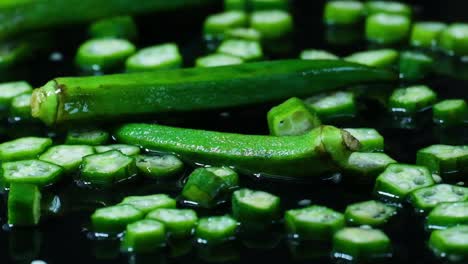 Okra-Vegetal-En-Rodajas-Cayendo-Sobre-Una-Superficie-Negra-Húmeda,-Vista-De-Estudio