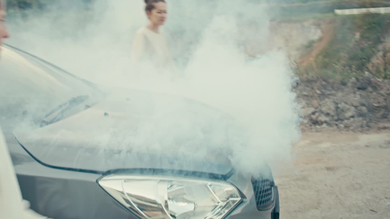 People dealing with a smoking car engine breakdown on the road.