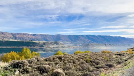 A serene drive through Queenstown, New Zealand, showcasing vibrant autumn foliage, a tranquil lake, and majestic mountains under a clear sky