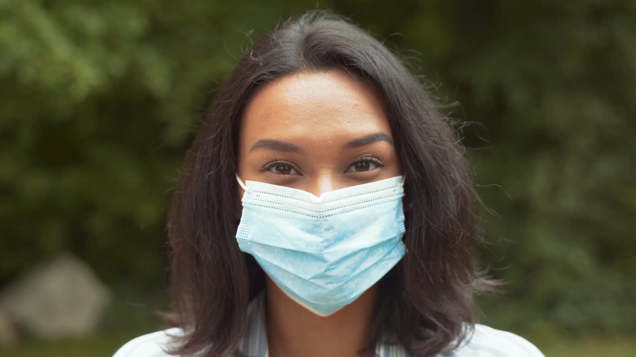 retrato de una chica guapa sonriendo con mascarilla médica al aire libre, mirando a la cámara, tiro de cerca