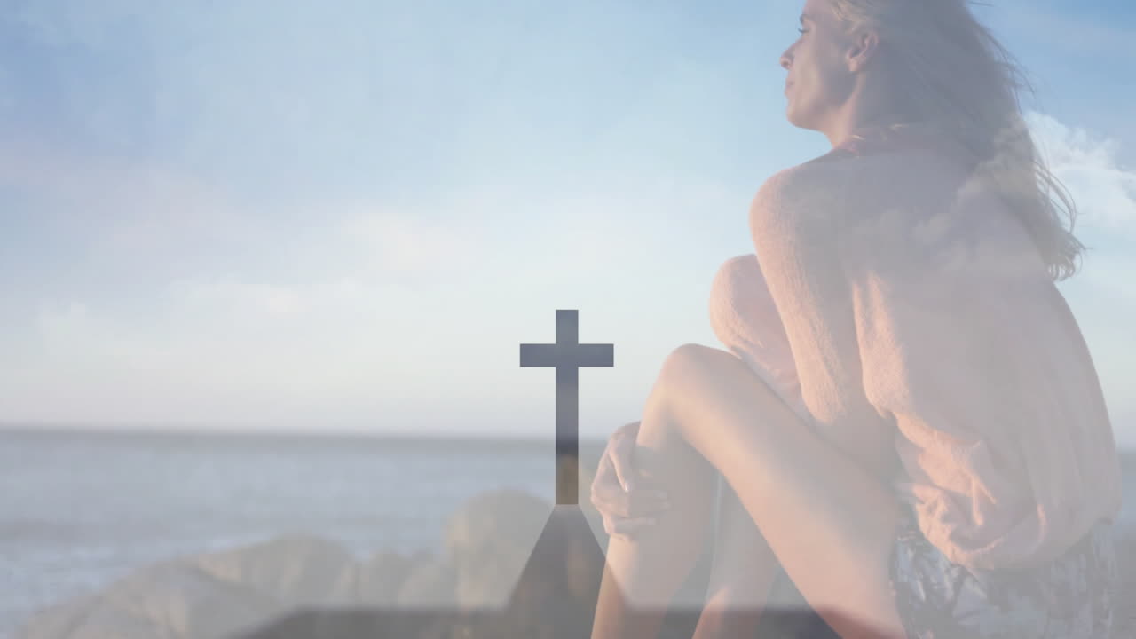 Sitting on rocks by ocean, woman with cross symbol in animation overlay
