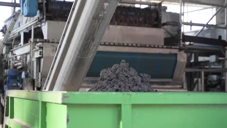 Sludge-and-dirt-dropping-into-bin-from-conveyor-in-wastewater-treatment-plant