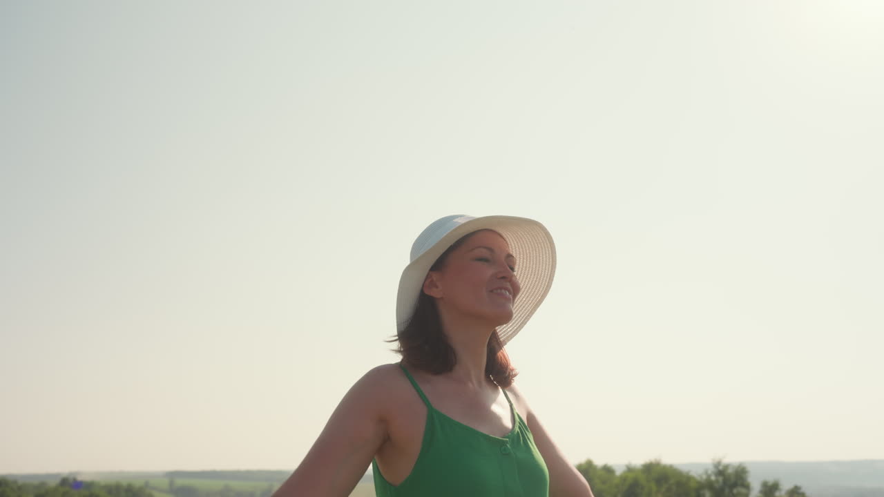 joyful lady in white sunhat dances gently under clear sky in tall grassy field, smiling warmly in sunlight as breeze lifts her hair, embodying carefree spirit of summer in peaceful countryside landscape