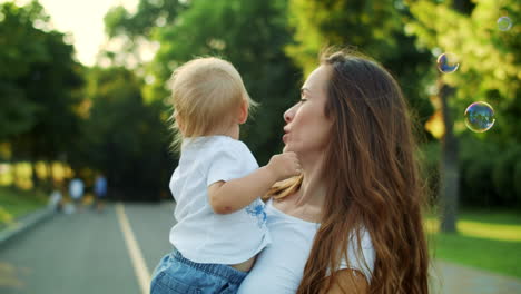 Madre-Hablando-Con-Su-Hijo-En-Las-Manos.-Niño-Mirando-Pompas-De-Jabón-En-La-Calle