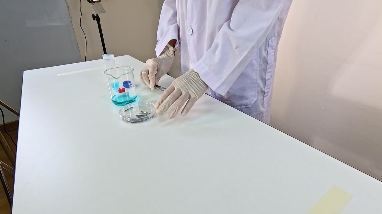 A scientist in a lab coat conducts a copper sulfate solution experiment on a white table under bright lighting