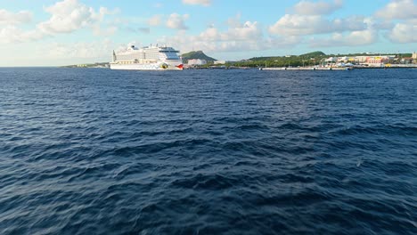 drone push in above rolling shimmering water with cruise ship docked in port