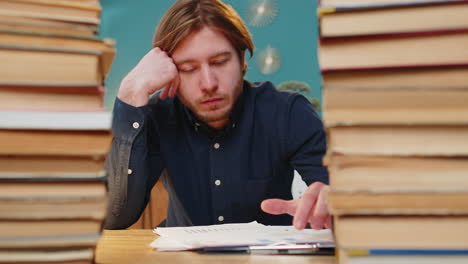 exhausted businessman moving stacks of books and reviewing documents reports while drinking coffee