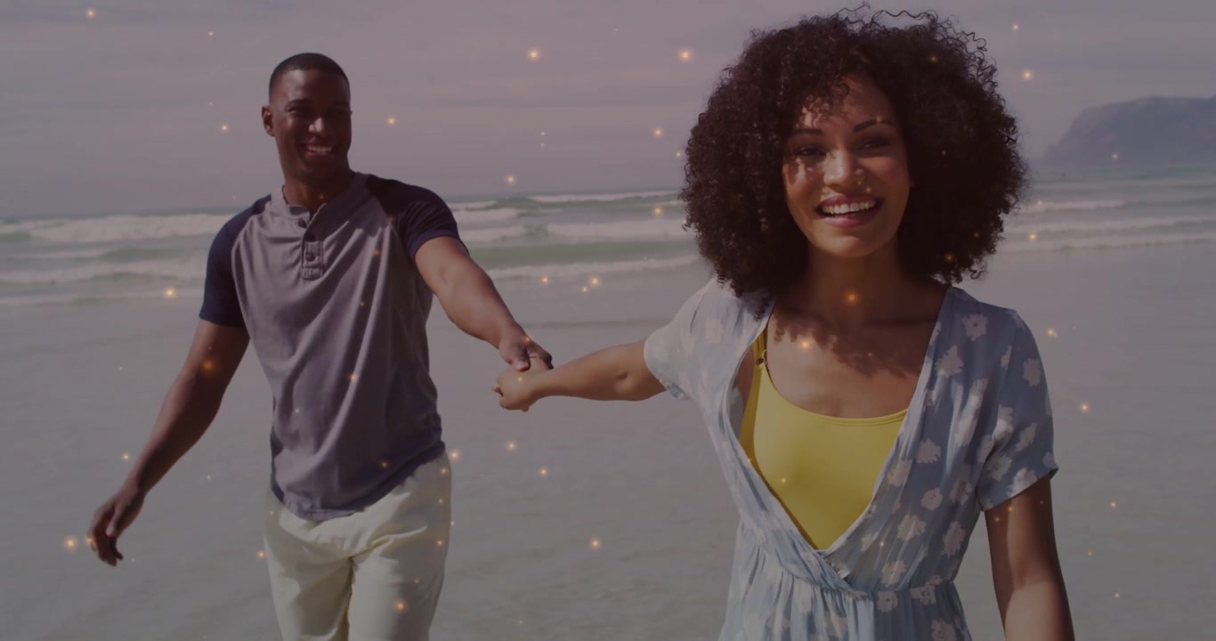 Coppia che cammina verso la fotocamera, con la donna che precede, tenendosi per mano, in un momento romantico sulla spiaggia