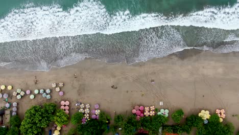 Foamy-ocean-waves-hitting-sandy-beach-of-Kuta,-aerial-top-down-descent-view