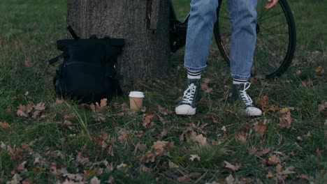 person with backpack, bicycle, and coffee cup in park