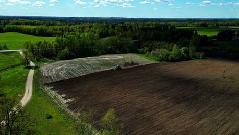 Vista-Aérea-Del-Campo-Agrícola,-Temporada-De-Siembra-De-Semillas-En-Letonia-Rodeada-De-Majestuosos-Bosques