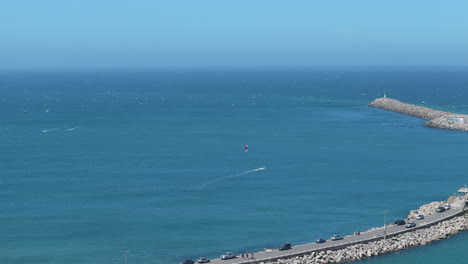 tracking drone shot of kite boarder in water next to coastal barrier at necochea, argentina. blue calm ocean makes main scene subject. shot 4k-60fps.