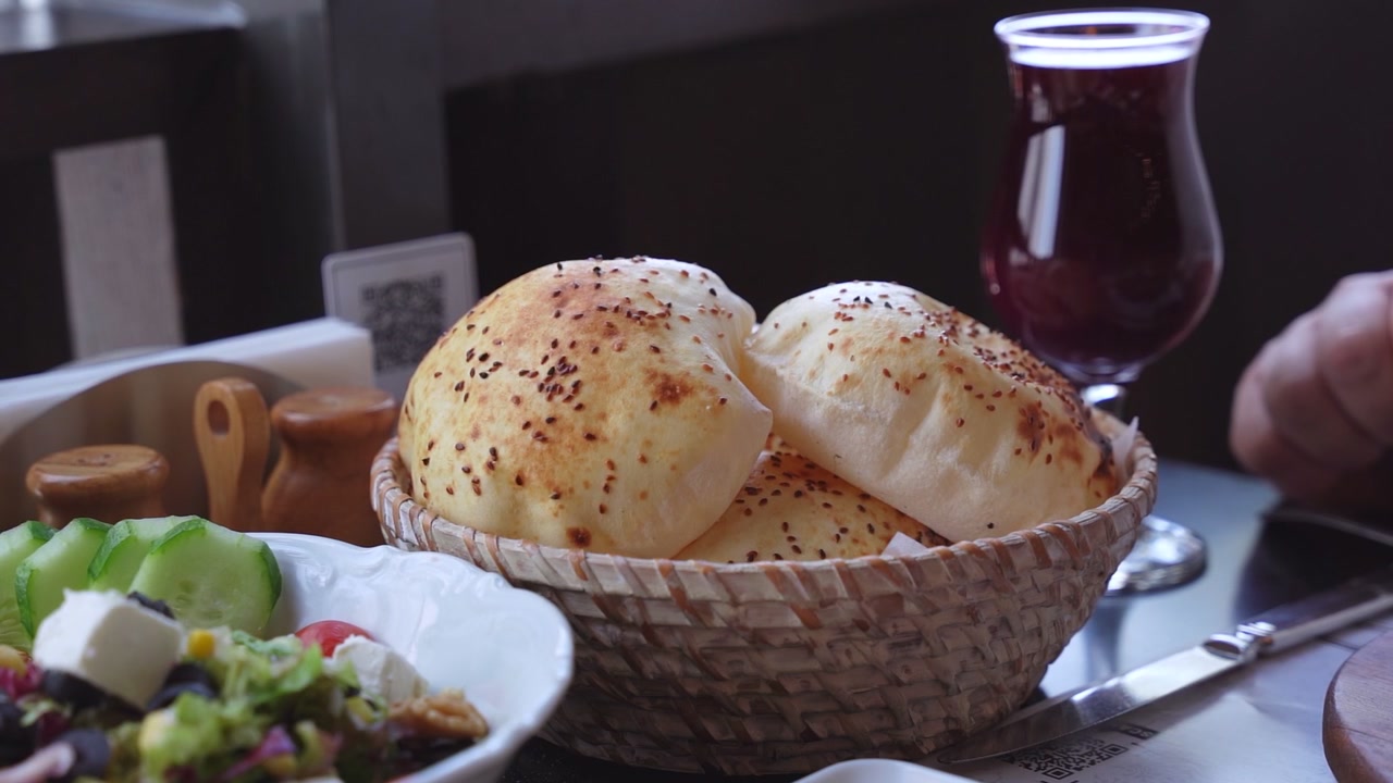 Close up of warm sesame-seeded flatbread in a wicker basket served with a fresh feta salad and a cold red fruit juice in a restaurant. Professional hospitality and culinary lifestyle footage.