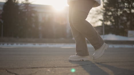 young woman moving with rhythm across sunlit pavement in white boots and winter pants, foot taps creating energetic winter beat on urban asphalt stage under warm glowing sunset light