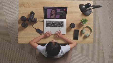 top view of asian woman editor having a backache while sitting in the workspace using a laptop next to the camera editing photo of a woman at home