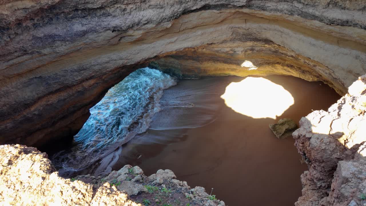 Slow-motion waves entering Benagil Cave with sunlight beam