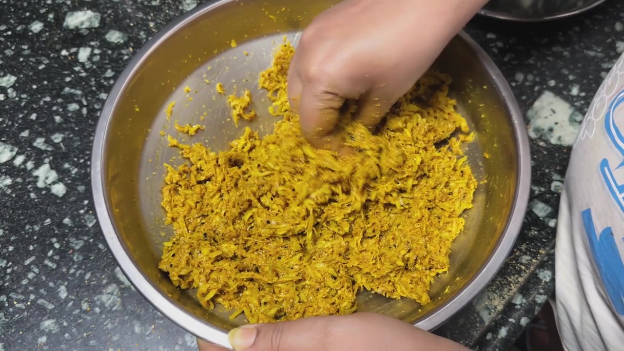 Static close shot of hands mixing shredded raw mango with spices and mustard oil inside a steel bowl during homemade Indian pickle preparation on a kitchen countertop