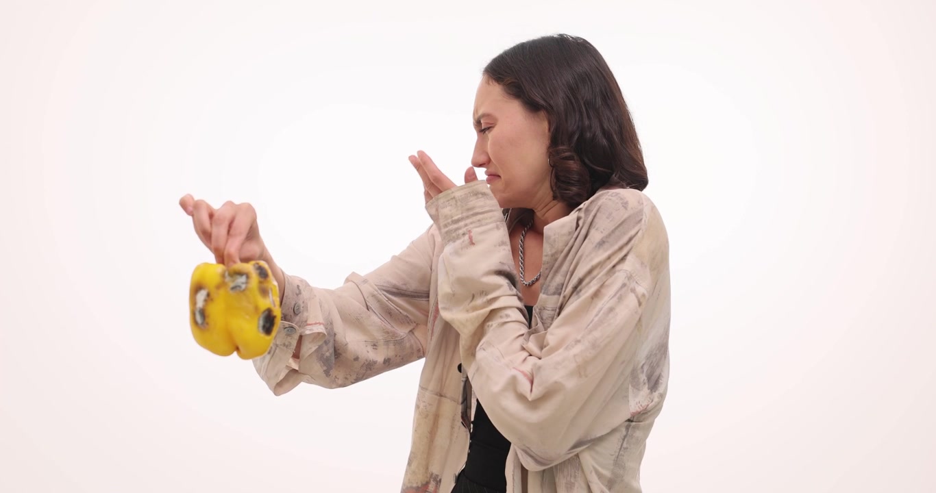 Woman holds rotten bell pepper covered with green mold in hand