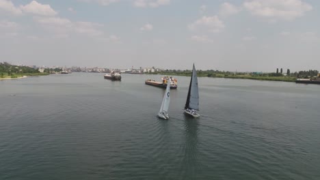 barcos de vela en un río con buques de carga en el fondo