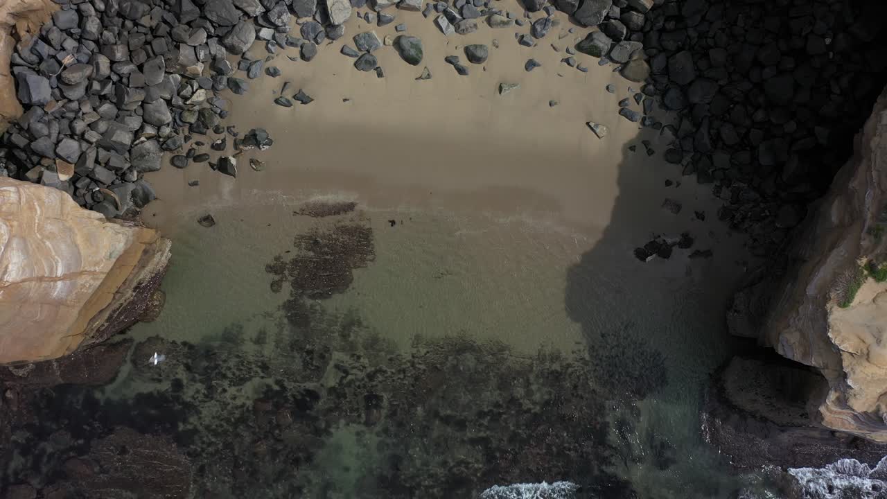 Luftfoto fra drone fanger den betagende skønhed af en strand omgivet af tårnhøje klipper, mens dronen langsomt stiger op og afslører den spektakulære kystlinje fra oven
