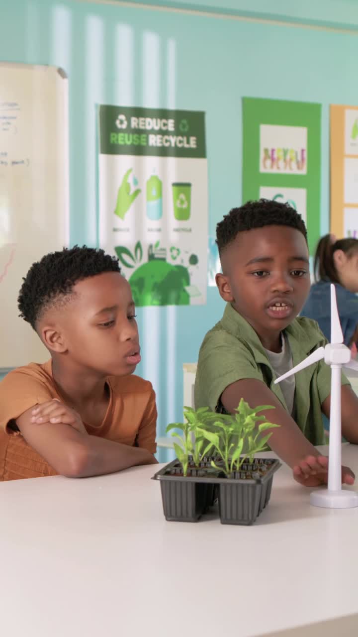 Vertical video: Reacting to demo, green-shirt boy adjusting wind turbines in class, with tablet